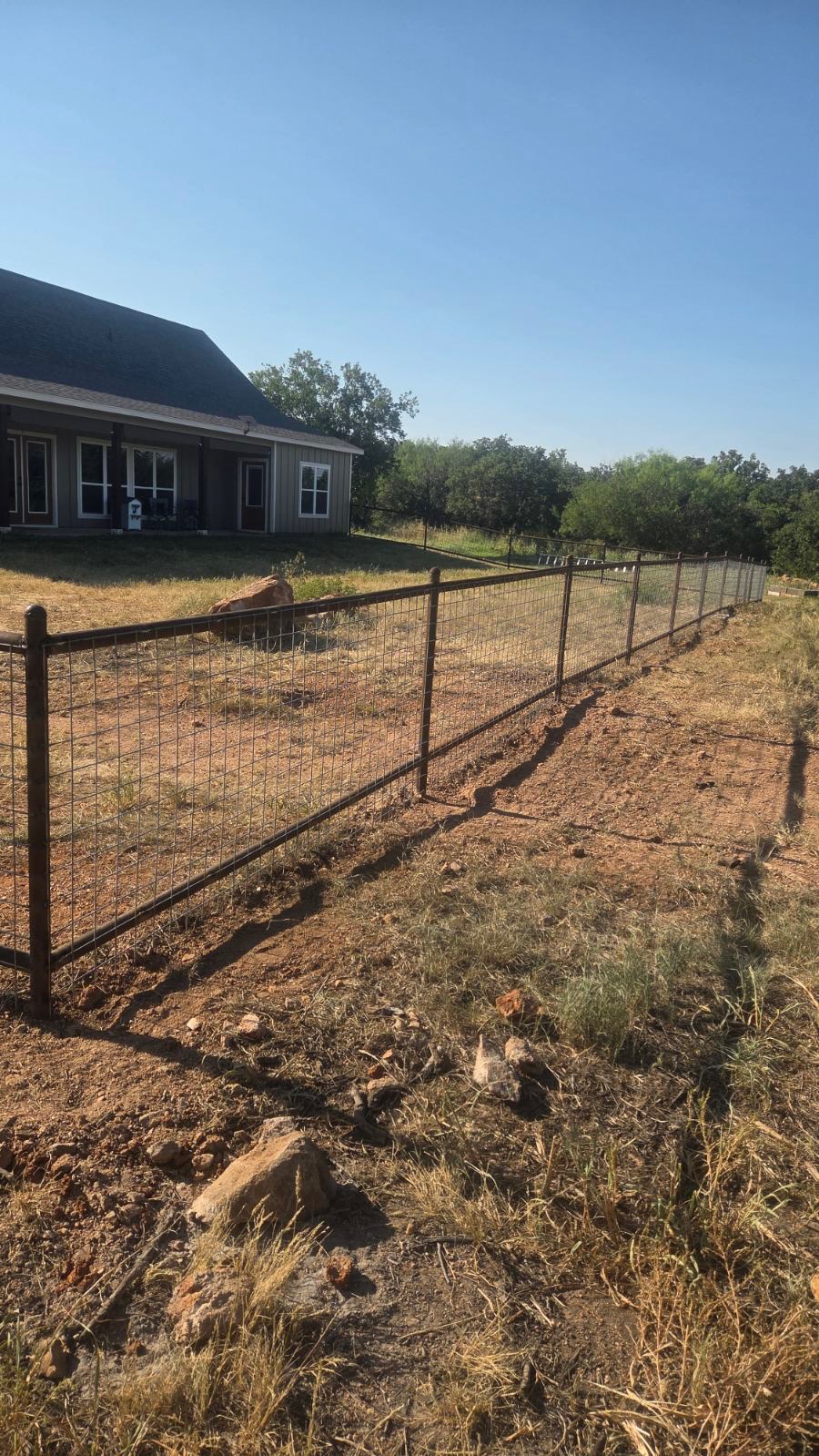 Long welded pipe fence run with 4x4 wire panels beside a Texas home