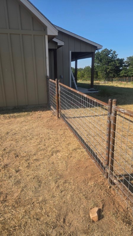 Two-rail pipe and wire-panel fence installed along a ranch outbuilding