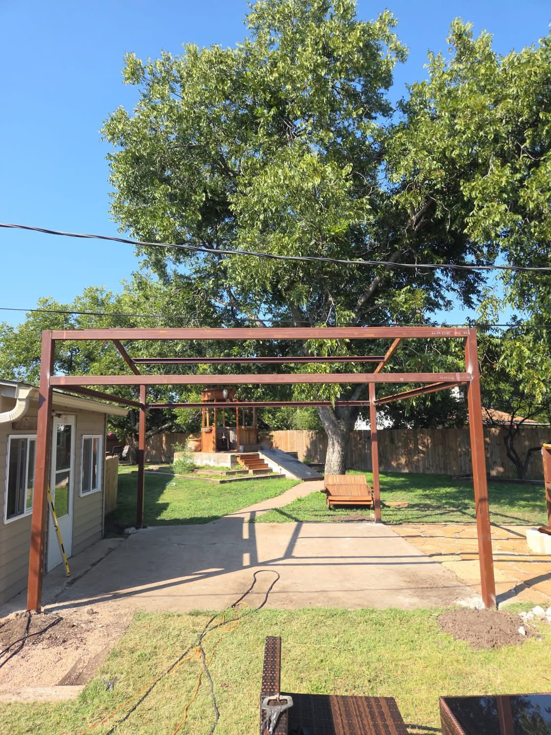 Wide view of a steel patio-cover frame built over a Texas backyard slab