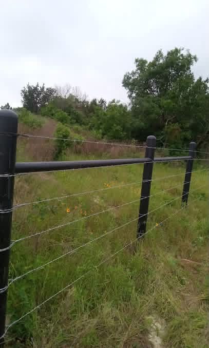 Black pipe top rail with field wire installed across a green Texas pasture