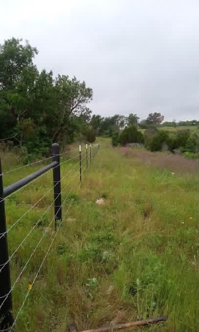 Long black pipe-and-wire ranch fence following a Texas pasture boundary