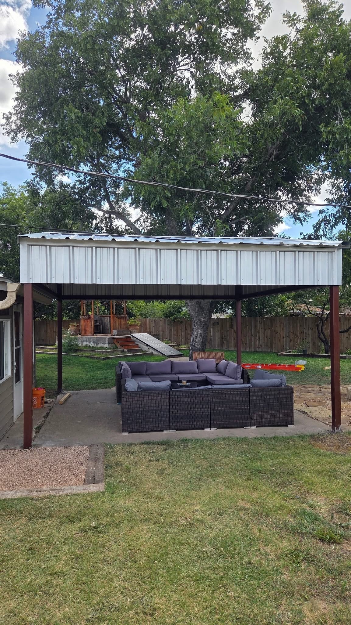 Open-sided metal patio cover with steel posts and a finished outdoor seating area