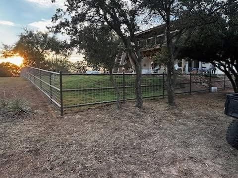 Pipe-and-wire ranch fence enclosing a Texas acreage property at sunset