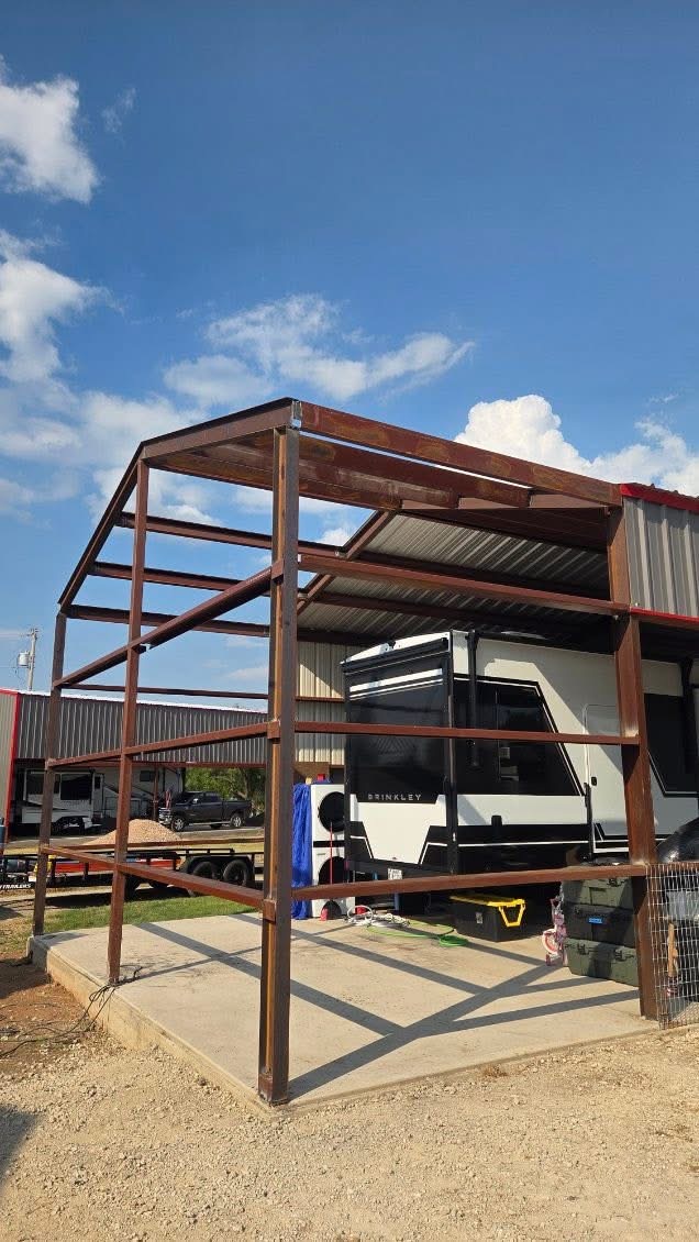 Welded steel frame for a custom RV carport addition beside a metal building in Texas