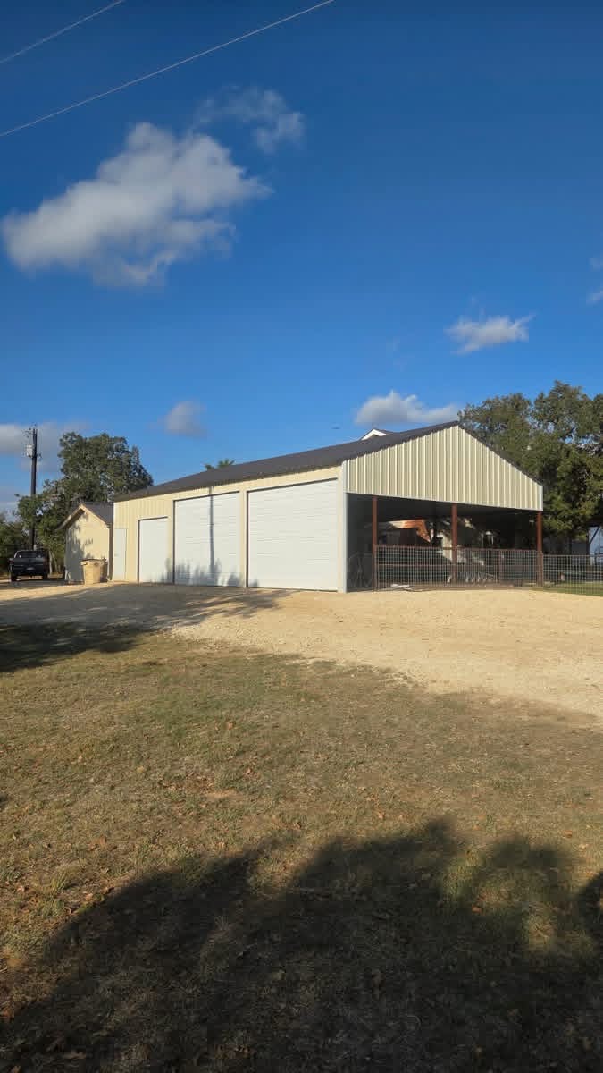 Three-bay metal shop with roll-up doors and covered equipment parking in Texas