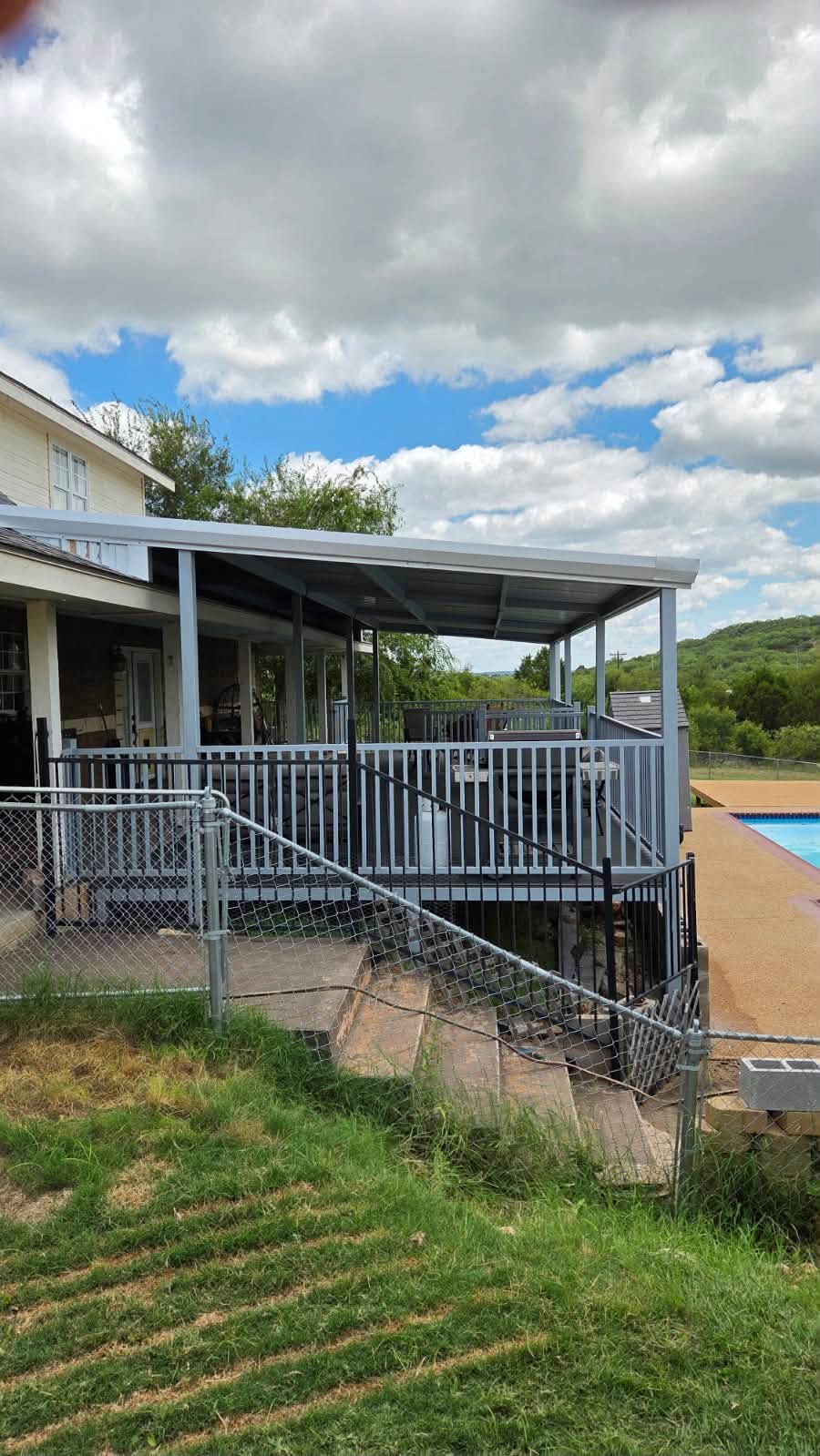 Exterior view of a steel-framed covered deck and metal patio roof beside a pool
